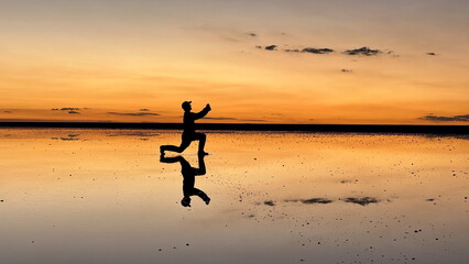 Silhouette of a Man Kneeling and Offering a Flower on Uyuni Salt Flat at Sunset, Bolivia