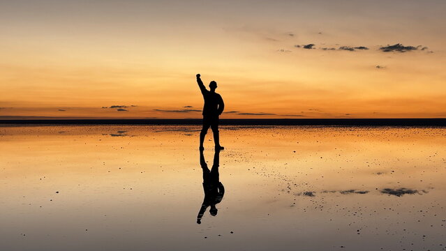 Silhouette of a Man Raising His Fist at Sunset on the Mirror Surface of Salar de Uyuni, Bolivia