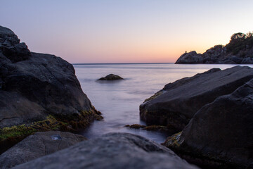 Fototapeta premium A stunning view of large, jagged rocks on a tranquil sea shore, with a small stream of calm water flowing between them, a perfect image for conveying themes of nature, coastal travel, or serene landsc