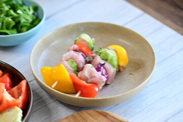 Close-up view of a raw chicken skewer prepared for roasting. Fresh pieces of chicken meat threaded onto a wooden stick along with colorful vegetables, creating an appetizing composition on a kitchen