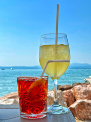 Refreshing summer cocktails by the seaside. A red aperitif and a white wine spritz against the backdrop of sky and water. Concepts of vacation, relaxation, and summer lifestyle