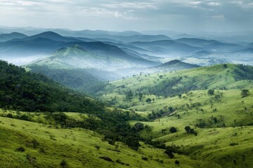 Fototapeta premium Lush Green Hillsides with Blue Mountain Range on Misty Day Under Cloudy Sky