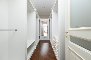 Bright hallway features white walls and wood flooring, showcasing empty closets and a clean aesthetic in a contemporary apartment. Natural light enhances the spacious feel.