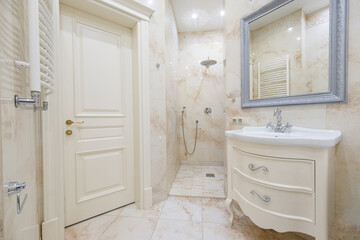 A beautifully designed bathroom showcases a spacious shower area and an elegant vanity. The light marble walls reflect soft lighting, enhancing the sophisticated ambiance.