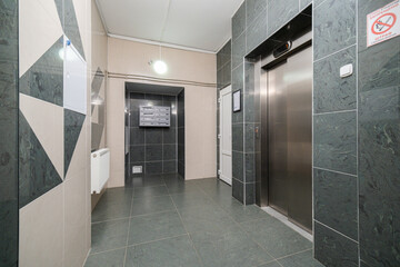 A contemporary elevator lobby showcases elegant dark tiles, sleek mailboxes, and a well-lit atmosphere, highlighting its functionality in a residential urban environment.