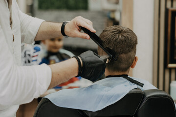 Smiling little boy sitting at barber shop, while hairdresser styling his hair.
