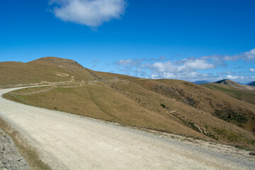 Winding Dirt Road Through Rolling Hills Under Blue Sky