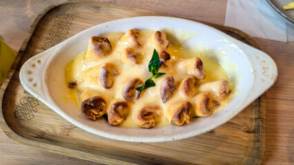Baked Dumplings with Creamy Cheese Sauce in Ceramic Dish. Golden baked dumplings covered in rich cheese sauce and garnished with mint, served in a white ceramic dish.