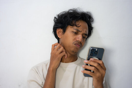 A relaxed Asian man holds his phone, rubbing his neck.