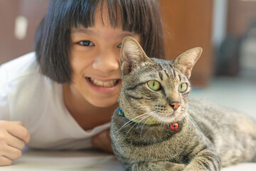 Asia kid girl playing with Thai cat. Little happy Asian child lay down softly touching her pet at head.Love Your Pet Day.Random Acts of Kindness Week.Be kind to Animals