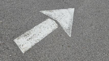 White painted arrow on asphalt road surface, representing direction and navigation in transportation contexts.