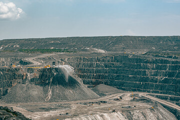 Wide view of a Canadian open-pit gold mine in Malartic, Quebec, showing heavy machinery and active dust control with water spraying on crushed rock. Industrial mining landscape.
