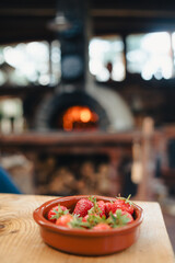Bowl of red strawberries at the table, pizza oven in the background