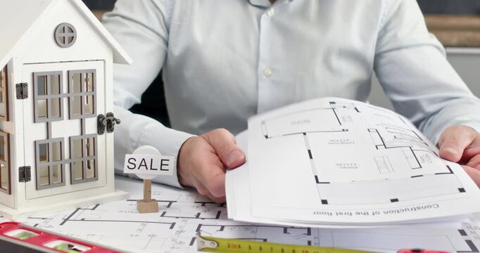 Man office worker flips through stack of detailed room sketches and discusses property features with partner. Partners shake hands to finalize agreement over drawings