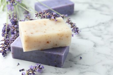 Soap bars and lavender flowers on white marble table, closeup. Space for text