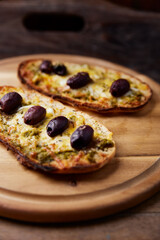 Bruschetta with mozzarella and cheddar cheese, olive pesto and kalamata olives. on wooden background. Soft focus. Close up	