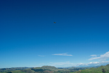 Airplane Flying Over Green Hills Under Clear Blue Sky