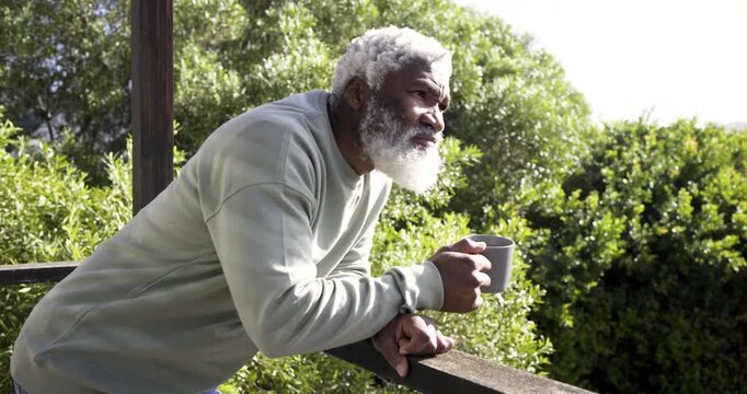 At sunrise, senior African American man stepping onto balcony with coffee mug, sipping, reflecting
