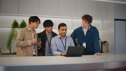 Focused diverse office people and young highschool student intern working at startup. Colleagues collaborating on project with laptop in modern kitchen