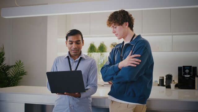Two diverse people in modern startup office. thoughtful highschool student or intern gets mentorship while looking at laptop with colleague during project discussion