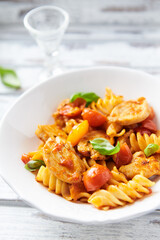 Pasta with chicken breast, cherry tomatoes and fresh basil. Bright wooden background. Close up.