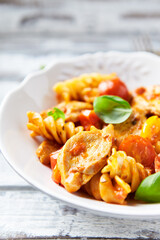 Pasta with chicken breast, cherry tomatoes and fresh basil. Bright wooden background. Close up.
