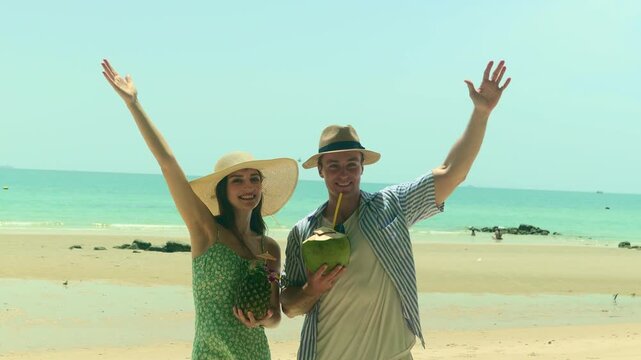 Honeymoon couple enjoying a summer beach vacation drinking coconut and pineapple walking along beautiful beach smiling with the utmost happiness.