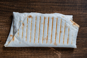 Delicious shawarma wrapped in lavash with filling on wooden background, closeup, top view. A perfect choice for a quick and satisfying meal. Texture of pita bread from the grill. Simple fast food