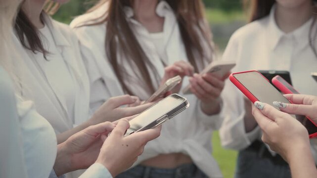A large group of lively young friends came together outdoors, clearly focused on their various smartphones