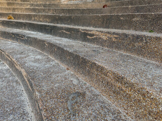 A low-angle view of weathered, curved concrete steps, showing their speckled texture and horizontal lines receding upwards, with a blurred natural background.