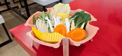 Organic vegetables, arranged in pink bowl placed on red table. Set of healthy vegetables : carrots, pumpkin, corn, mushrooms, green vegetables for use in shabu, sukiyaki, Thai BBQ. 5-color vegetables
