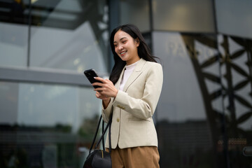 Smiling businesswoman using smartphone while walking near office building
