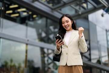 Fototapeta premium Young asian manager expressing joy and excitement after receiving good news on her phone