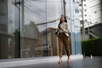 Young businesswoman walking in the city and using smartphone