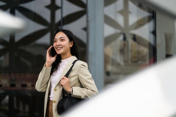 Smiling businesswoman talking on phone while walking near modern office building