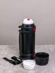An open black thermos with cups stands on the table