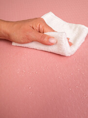 Close-up of a woman's hand wiping water drops off a yoga mat with a white cloth