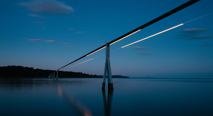Illuminated pipeline stretches across calm twilight water, reflecting serene beauty.
