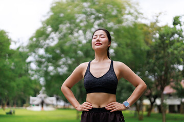 Young Asian sportswoman relaxing and breathing fresh air in a park