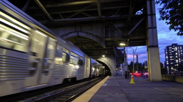 Urban Train Tunnel Entrance with Tracks Under Bridge Surrounded by Greenery and Evening Lights in Cityscape