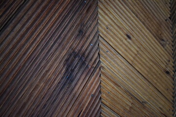 Close-up of a diagonal wooden panel with natural texture and visible grooves. Warm brown tones, aged surface, and clear wood grain detail