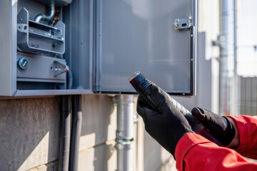 Electrical maintenance. An electrician's gloved hands hold a fuse next to an open outdoor electrical panel.