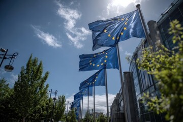 A vibrant scene of multiple European Union flags waving against a bright blue sky with fluffy clouds, surrounded by green trees and modern architecture.