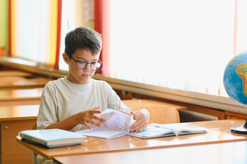 Schoolboy studying geography in classroom with globe on desk