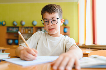 Schoolboy doing homework in classroom, concentrated pupil writing in notebook