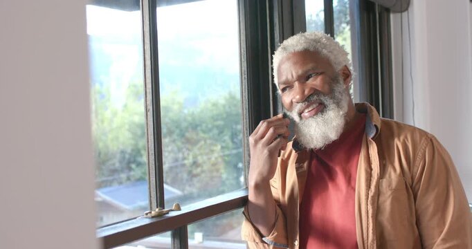 Mature African American man answering phone call by window listening, smiling over news copy space