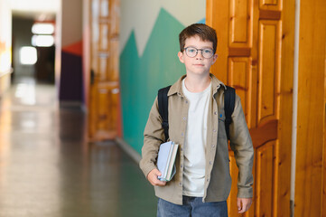 Schoolboy walking in school hallway holding books and wearing backpack