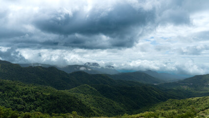 Naklejka premium Dramatic dark clouds loom over lush green mountains. With mist clinging to the peaks creating a moody and atmospheric natural landscape. Perfect for travel and wilderness themes.