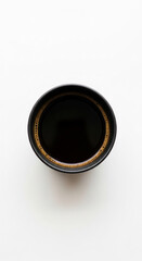 Overhead view of black cup filled with dark coffee, tan crema visible at the rim, simple white background showcasing the beverage, ideal for cafe menu or morning routine concepts