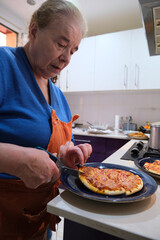 Grandmother cutting pizza with scissors on a plate, enjoying a cozy meal